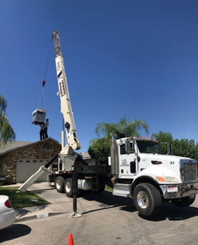 Crane truck lifting HVAC equipment at a home